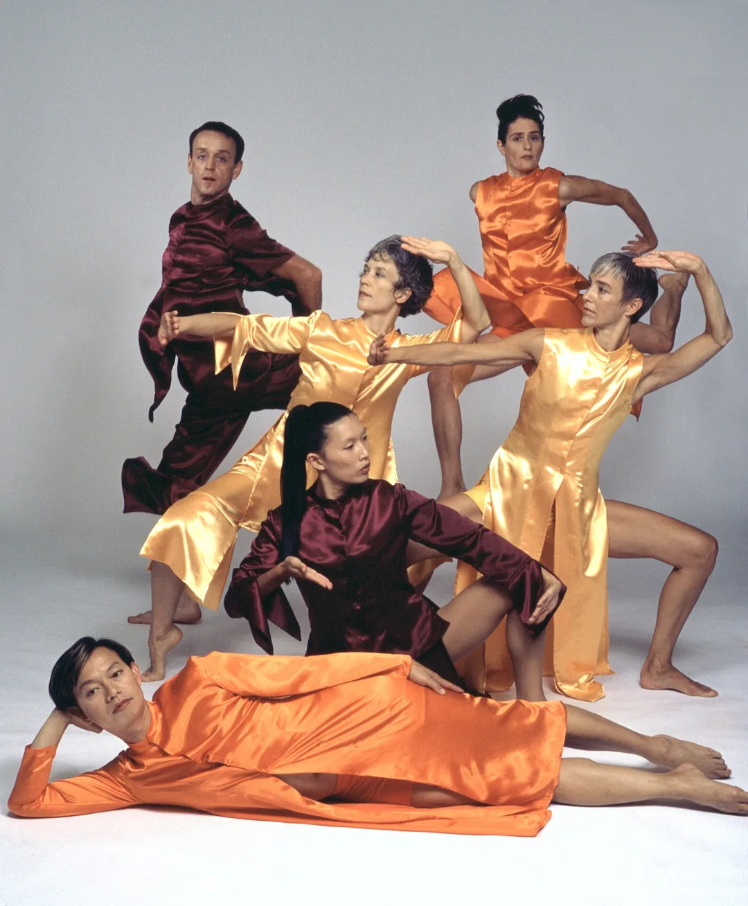 A dance ensemble wear shiny warm colors striking dramatic poses